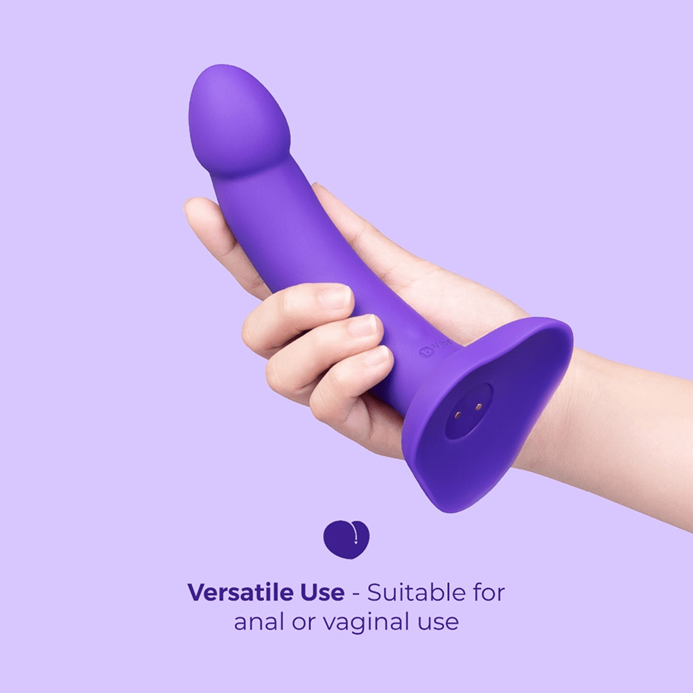 B-Vibe Vibrating Curved Strap-On Dildo Kit: hand holding curved purple dildo on a purple background with text that reads "Versatile use: suitable for anal or vaginal use"