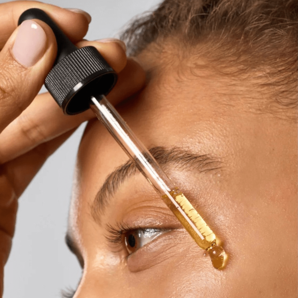 Close-up of a person applying a Kitsch Dermaplane Shave Oil dropper to the skin under their eye