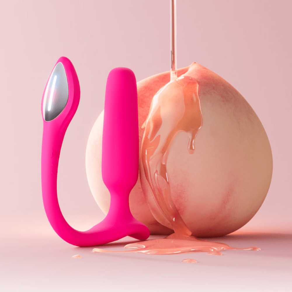 Lovense Lush Anal app-controlled butt plug next to a peach with peach-colored liquid dripping from above on a light pink background