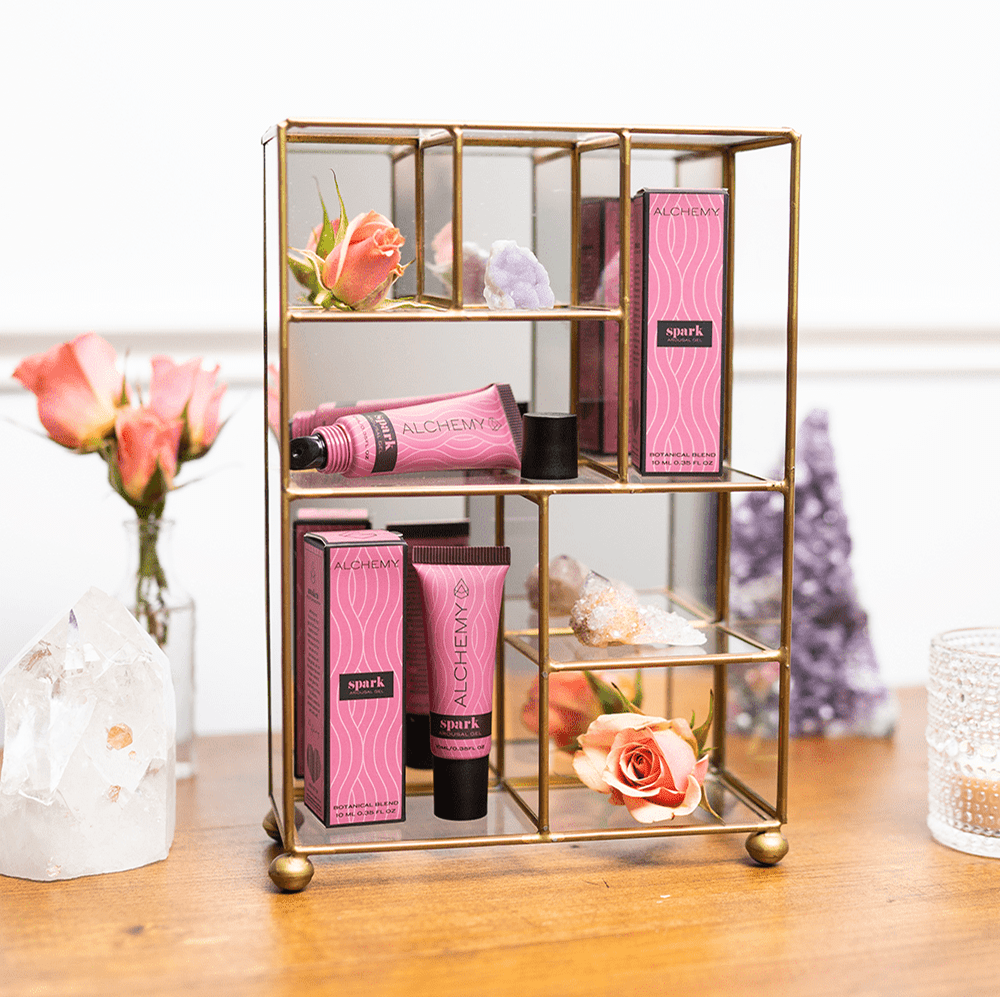Glass display cart with pink Alchemy Spark tubes and flowers on a wooden surface.