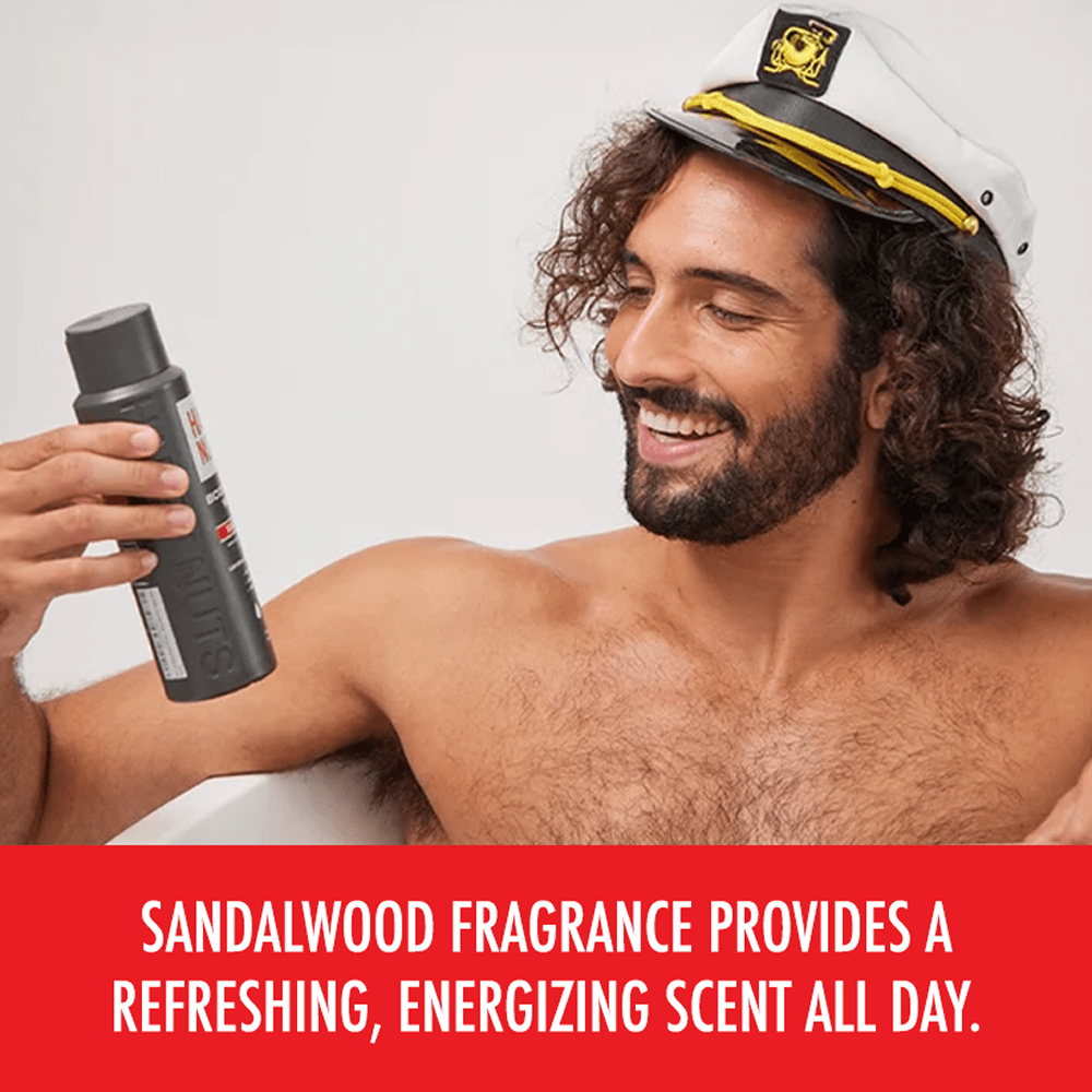 Man wearing captain's sailor cap holding bottle of Happy Nuts Nut & Body Wash on a light gray background with text that reads "Sandalwood fragrance rovides a refreshing, energizing scent all day"