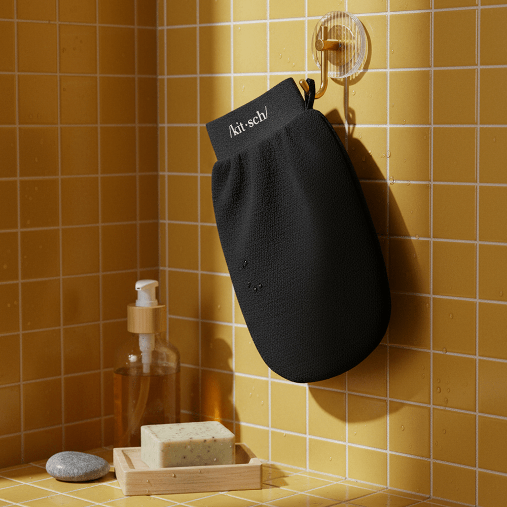Black Kitsch exfoliating glove hanging on a hook in an orange tiled shower with soap bar and bottle