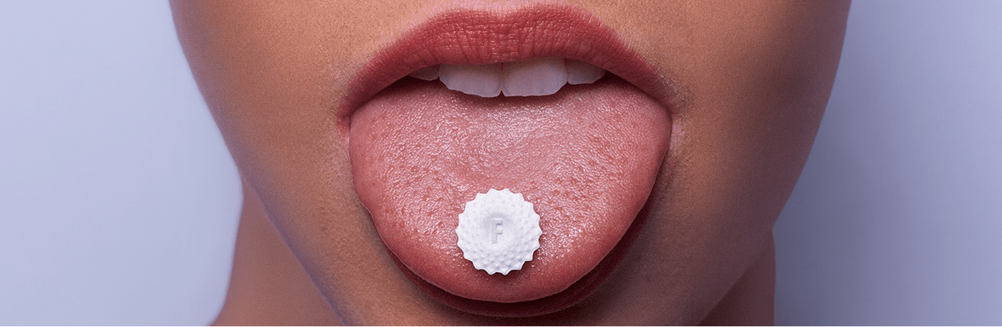 Cropped photo of Flintts Mints mint on a person's tongue with a light purple background