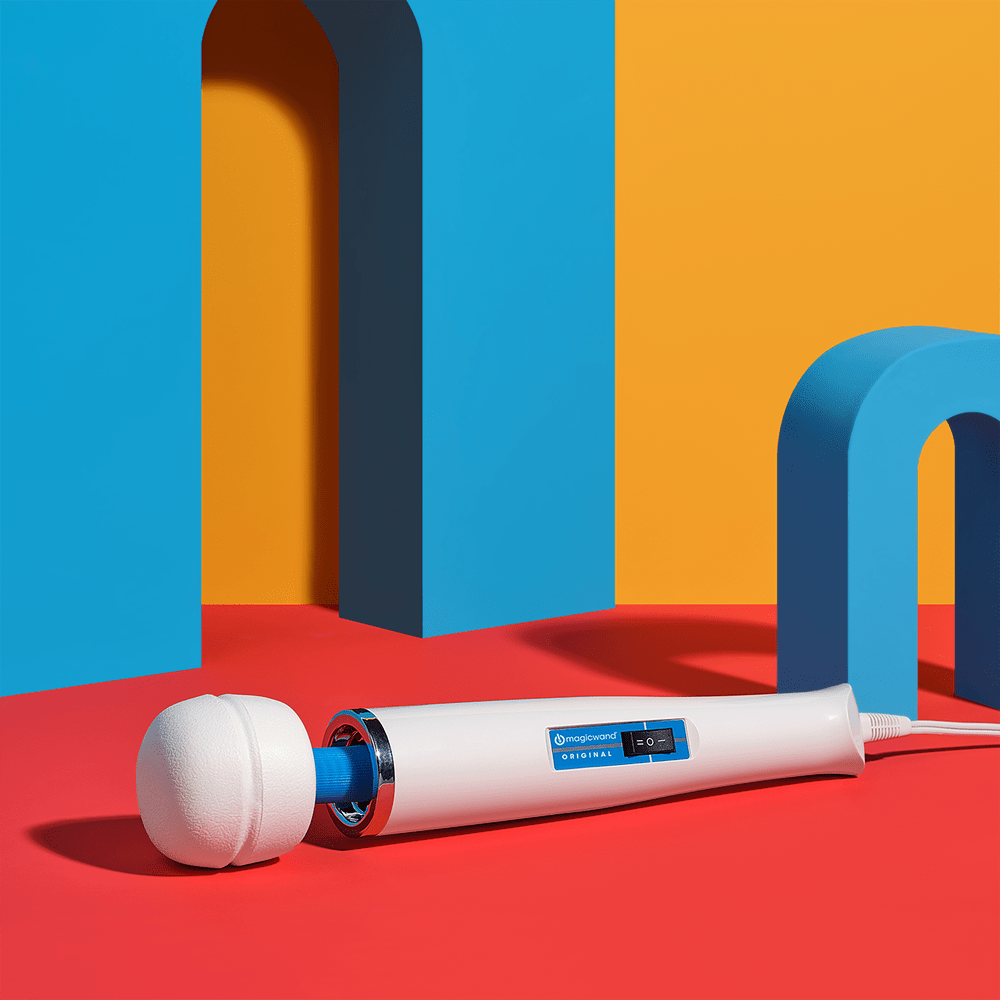 Photo of a Hitachi Magic Wand Original HV-260 plug-in wand massager on a red surface with blue and yellow geometric shapes in the background with overhead studio lighting