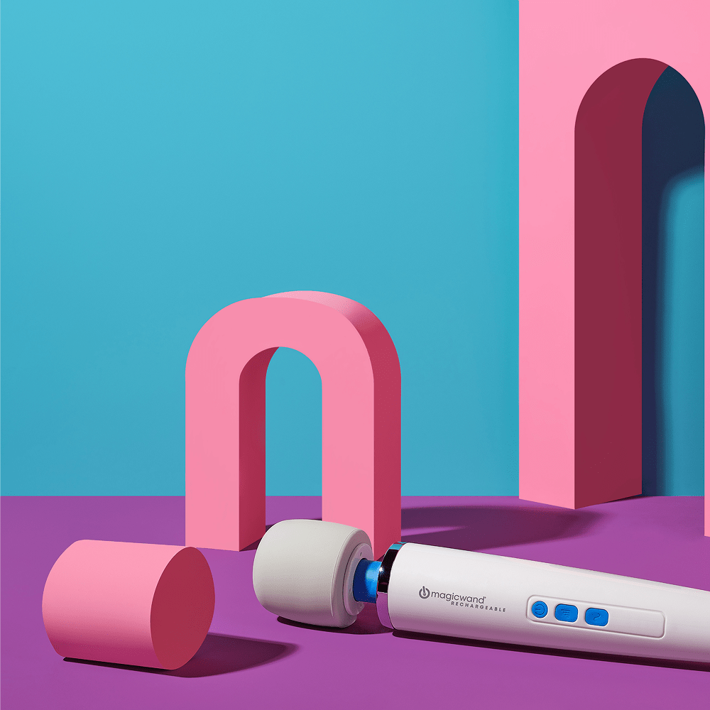 Hitachi Magic Wand Rechargeable HV-270 wand massager in a purple, pink, and turquoise 3D rendering environment with geometric shapes and overhead lighting