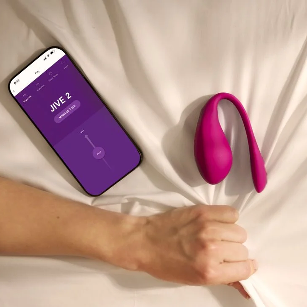 We-Vibe Jive 2: Photo of woman's hand gripping a tan bed sheet next to Jive 2 and a smartphone showing We-Vibe app screen