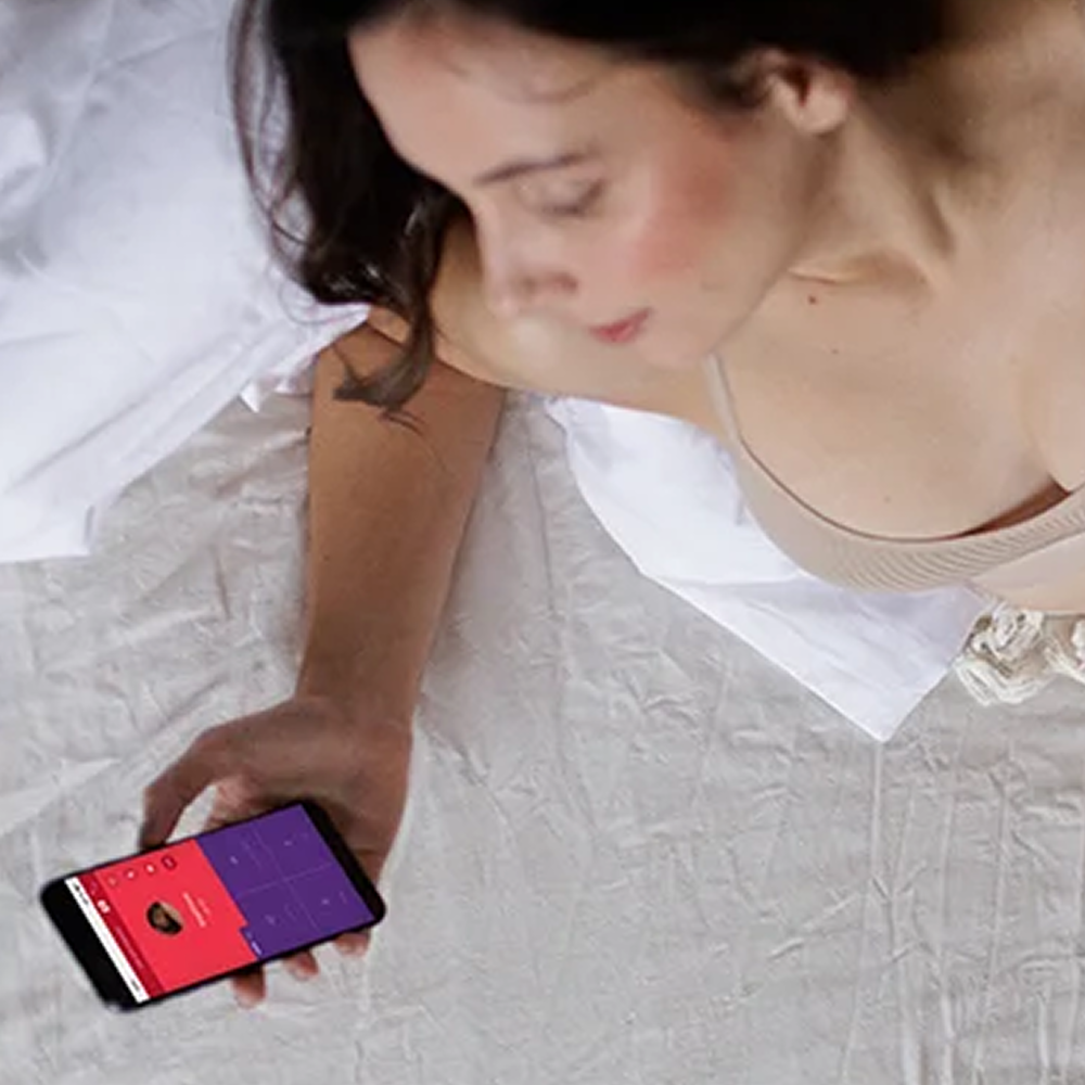 Woman holding smartphone showing a screen of the We-Vibe app