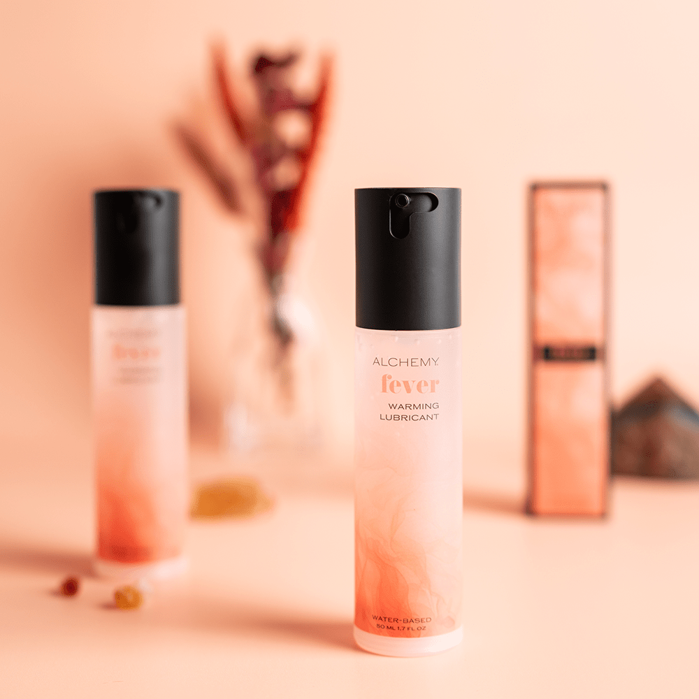 Two bottles of Alchemy Fever warming lubricant on a blurred background