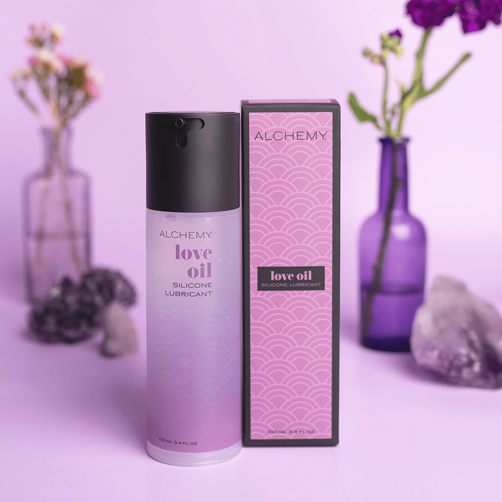 Alchemy Love Oil Silicone Lubricant with packaging on a purple background