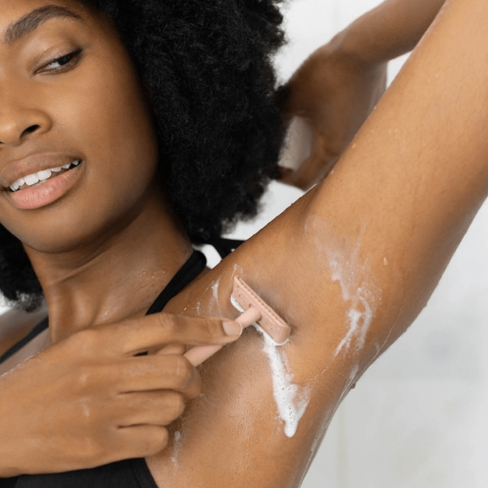 Woman shaving her armpit with a pink Kitsch razor on a white background