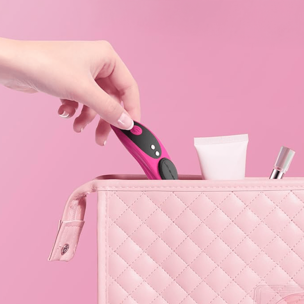 Woman's hand putting Lovense Ferri app-connected magnetic vibrating panty vibrator in a quilted handbag against a pink background