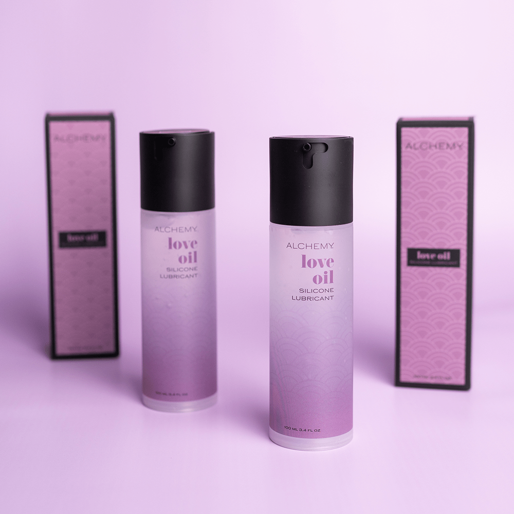 Two bottles of Alchemy Love Oil Silicone Lubricant on a purple background