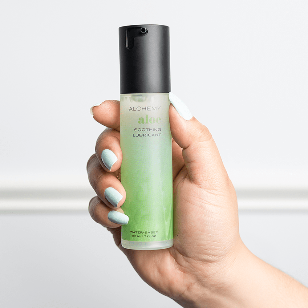 Hand holding a bottle of Alchemy Aloe soothing lubricant against a light background