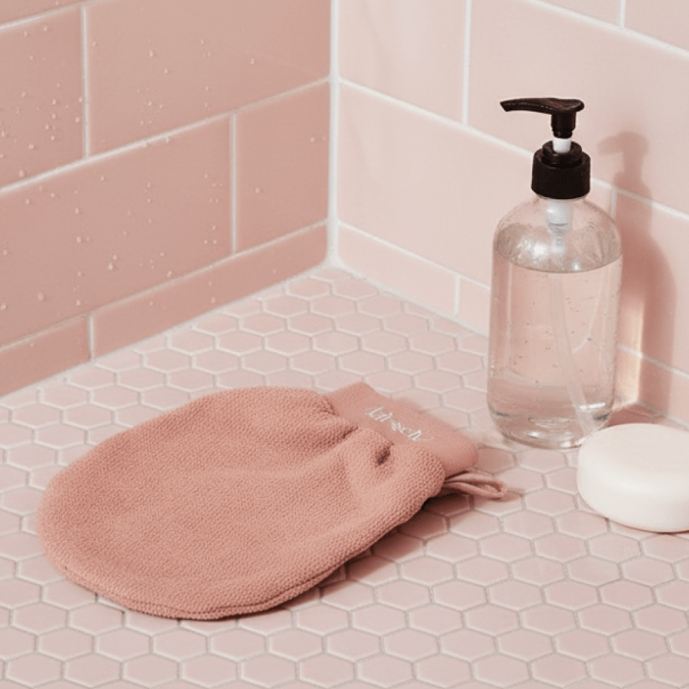 Pink Kitsch exfoliating glove and soap on a pink tiled bathroom counter