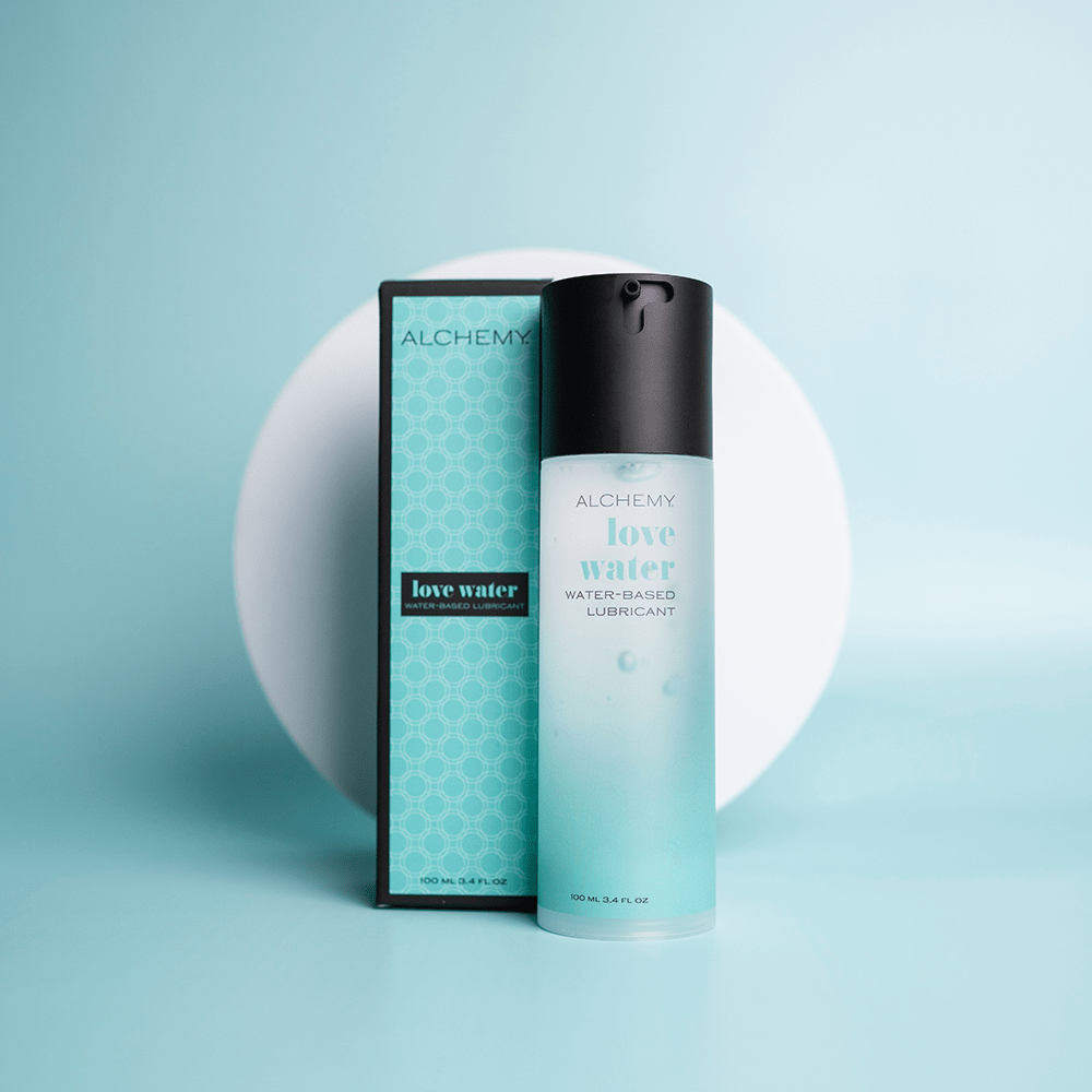 Alchemy Water-Based Personal Lubricant bottle and box on teal surface with a white circular shape in the background