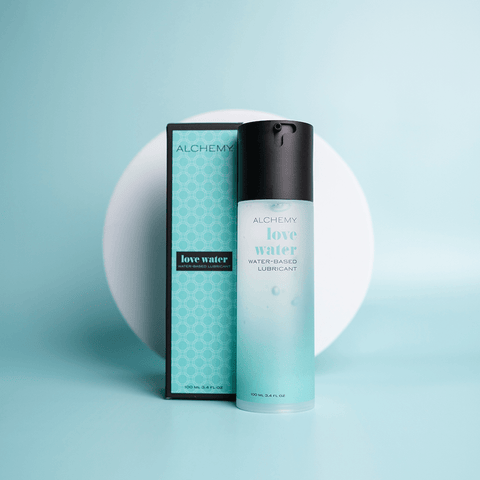 Alchemy Water-Based Personal Lubricant bottle and box on teal surface with a white circular shape in the background
