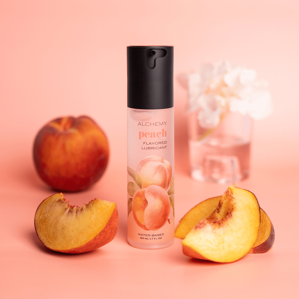 Alchemy Indulge – Peach Flavored Personal Lubricant bottle with peach slices and flowers