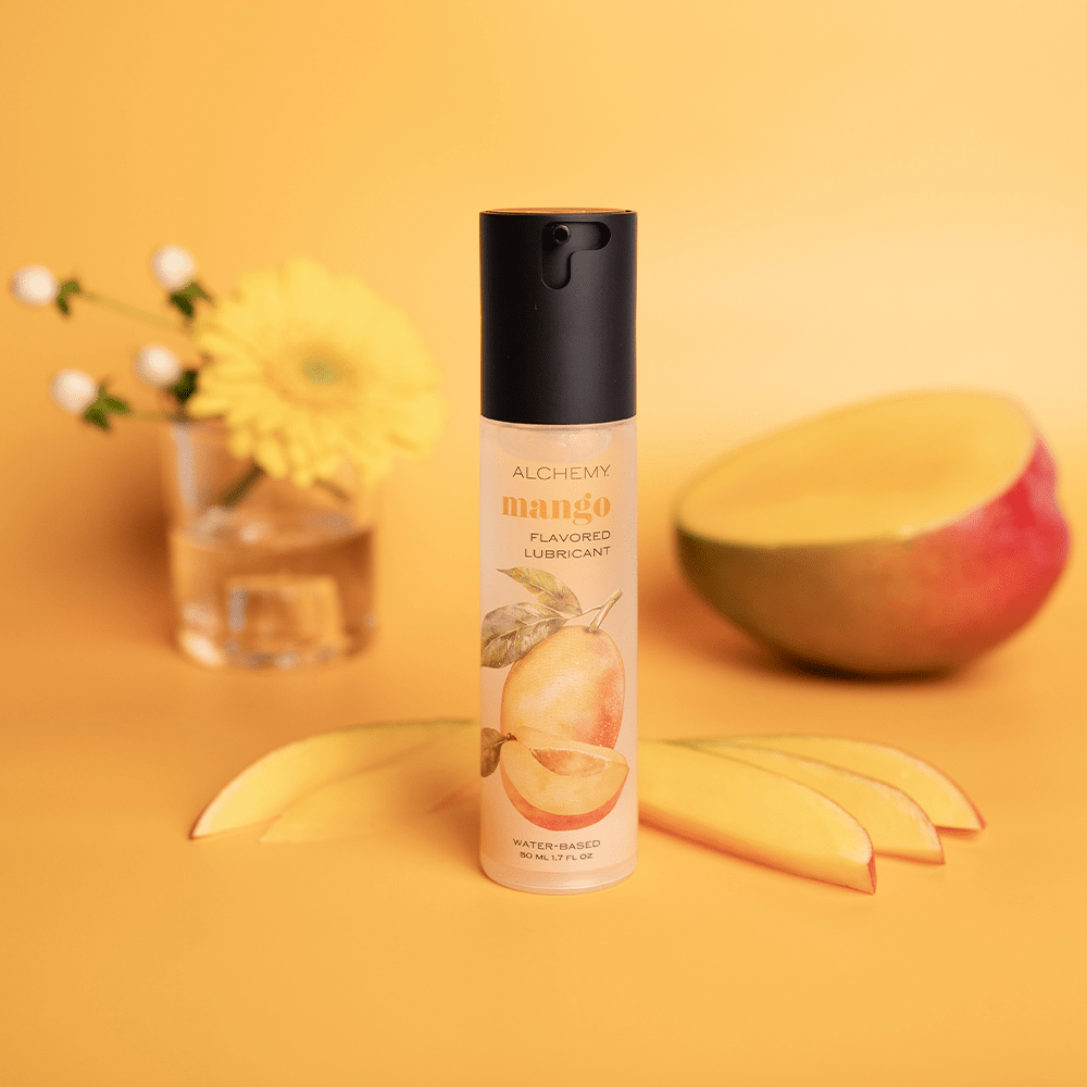 Alchemy Indulge – Mango Flavored Personal Lubricant bottle with mango slices and flowers