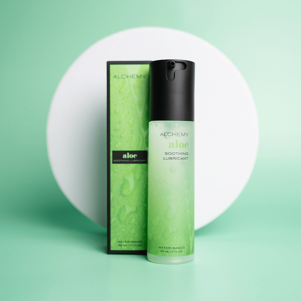 Alchemy Aloe Lubricant bottle and box on a green surface with a white circle in the background