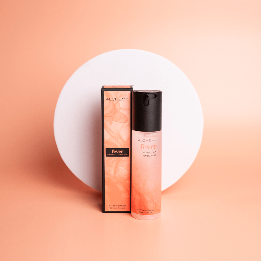 Alchemy Warming Personal Lubricant bottle and box on an orange surface with a white circle shape in the background