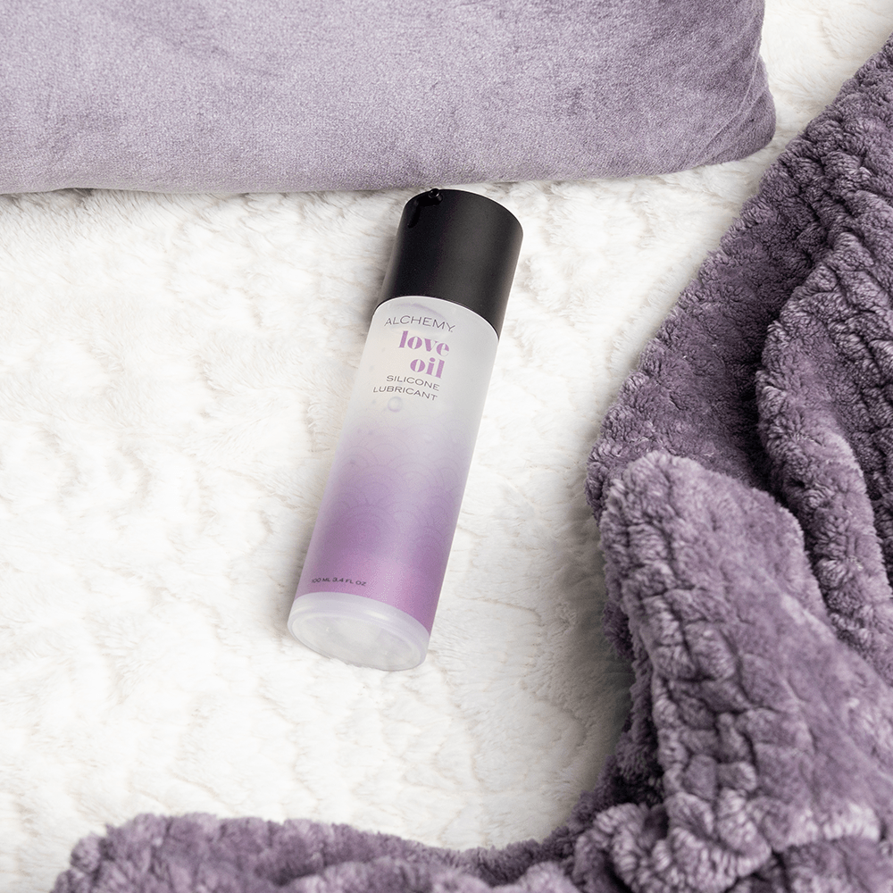 Alchemy Love Oil: Silicone-Based Personal Lubricant bottle on bed blanket
