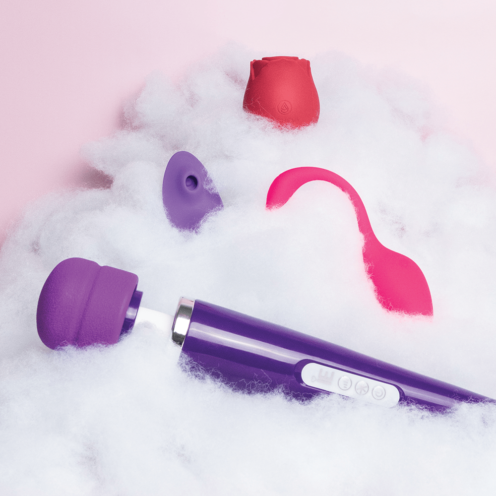 Amazing Intimate Essentials Alchemy Discovery Kit vibrator options: Alchemy Rosebud Luxury Air-Pulse Massager, Link Paige App-Connected Panty Vibe, Link Piper App-Connected G-Spot Vibe, and Intimate Essentials Rechargeable Love Wand on a fluffy cloud texture against a pink background
