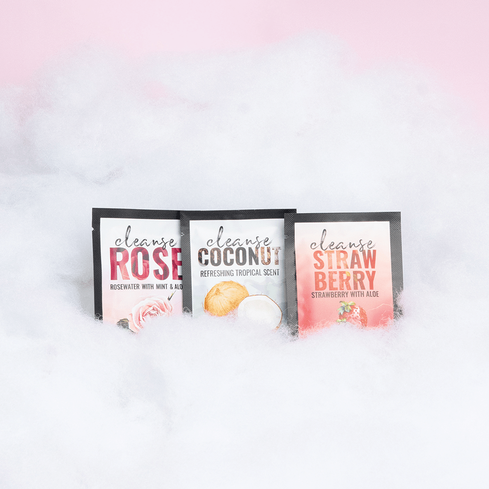 Amazing Intimate Essentials Alchemy Discovery Kit: Alchemy Cleanse Intimate Wipe packets on a fluffy cloud texture against a pink background