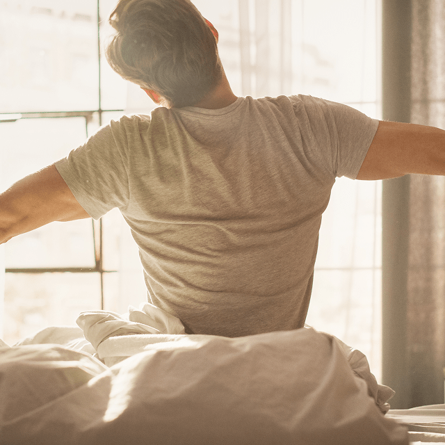 Man stretching in bed with natural light coming through the window