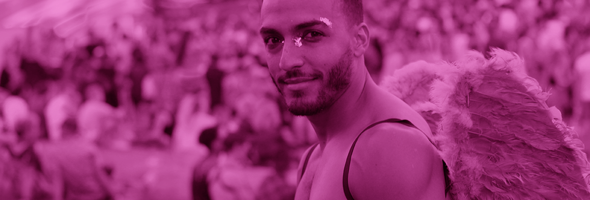 2025 Coachella-Inspired Pride Looks You Can Build Right Now: black and white photo of a young man at a Pride festival wearing wings with a pink color overlay