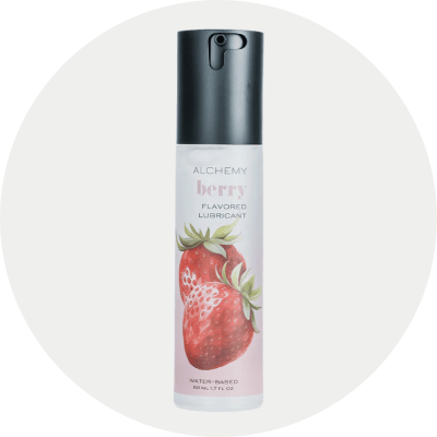 A bottle of Alchemy Berry Flavored Lubricant with a black cap and a white label featuring a strawberry illustration, centered on a light gray circular background