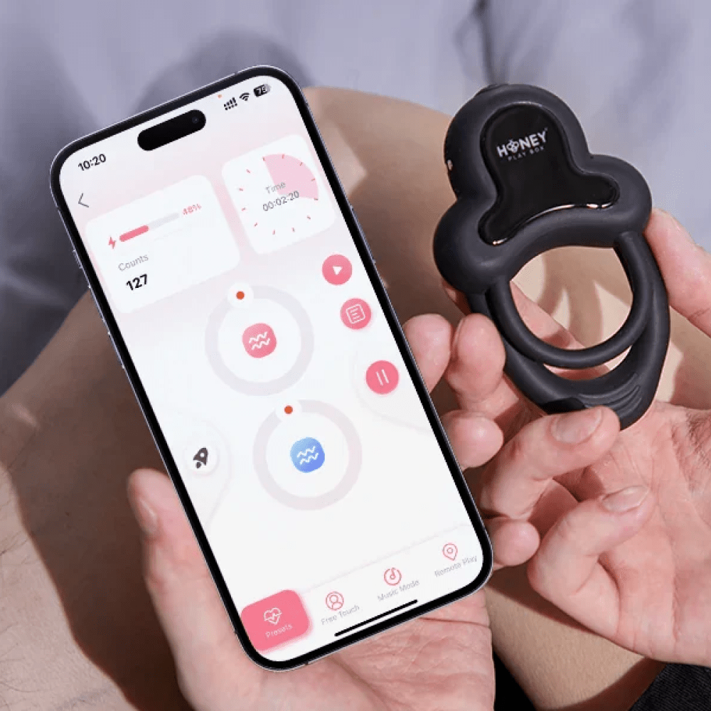 Honey Play Box Anello App-Controlled Vibrating Cock Ring - person's hand holding the product next to a smartphone showing the Honey Play Box app