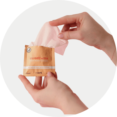 Person's hands holding Sweetums intimate wipe packaging in a light gray circle background