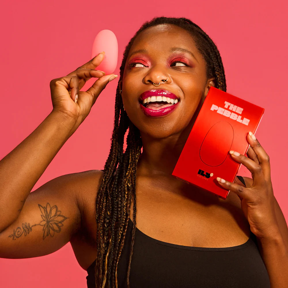 Woman holding a Je Joue ILY Pebble clitoral vibrator and its packaging against a pink background