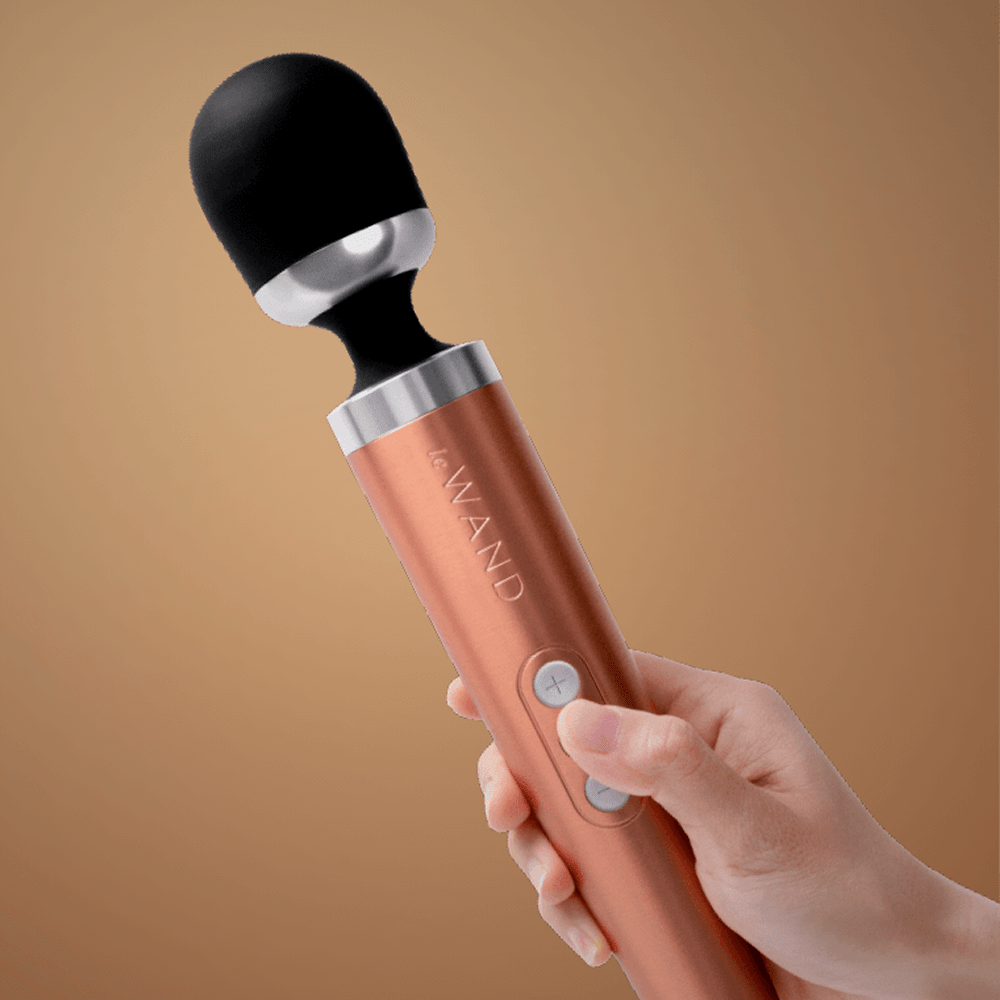 Woman's hand holding Le Wand Diecast Wand Massager in orange color with gold background