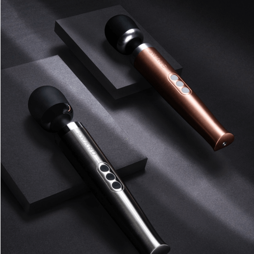 Two Le Wand Diecast Rechargeable Luxury Wand Massagers on charcoal gray tiered surface with studio lighting