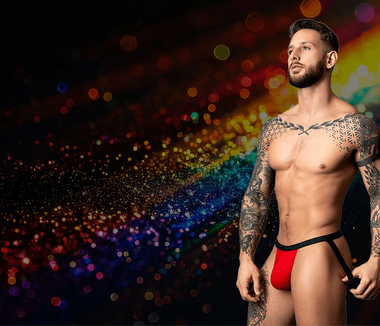 Man with tattoos wearing red underwear against a rainbow-colored blurred background