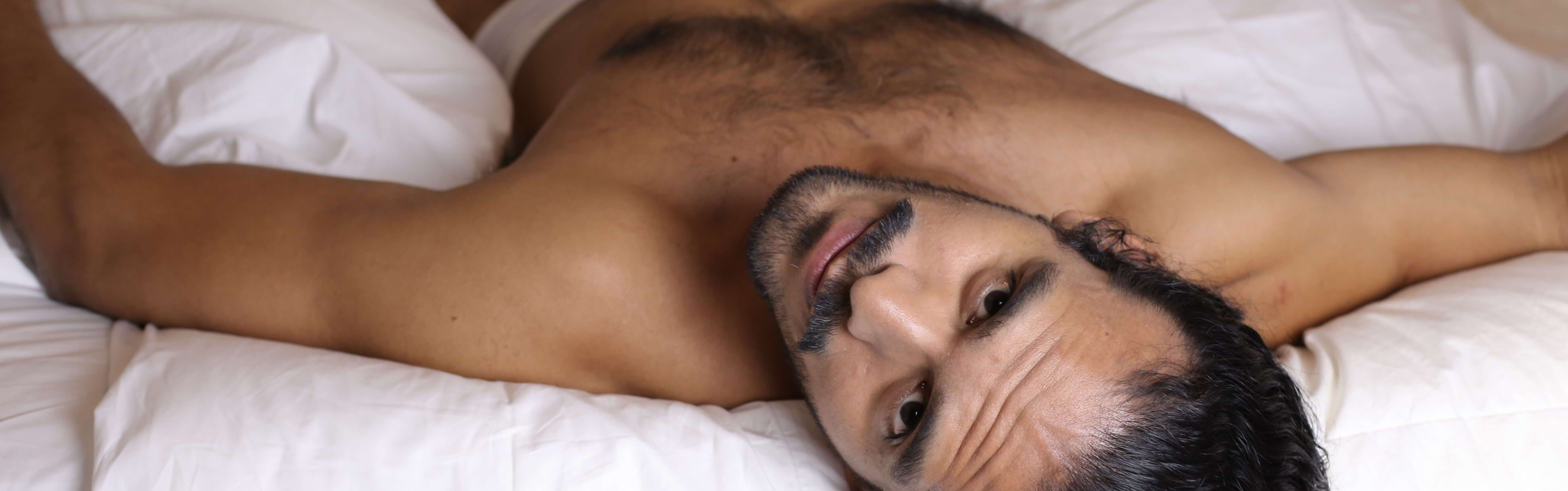 A young shirtless man lying in bed